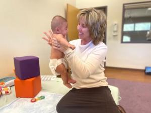 Valerie Pieraccini smiles while holding a baby in the therapy room.