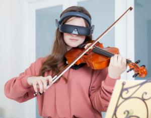 Young woman wearing eSight while looking at sheet music and playing the violin.