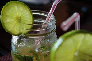 A mojito - a clear beverage with mint and lime in a mason jar with a red & white straw
