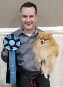 Bryan Harp holding Piper the Pomeranian and AKC Rally Novice 8th Place Rosette Award