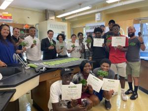 Students pose with teachers and staff while holding certificates and plants