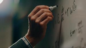 Photograph of a hand using a marker to write on a whiteboard.