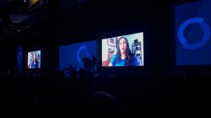 Picture of a large room with the lights off with bright screen in the center in front of the audience at Clinton Global Initiative 2022. The bright screen is a video in progress of Megha Desai, President of The Desai Foundation, talking about her CGI comm