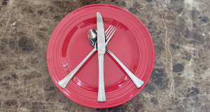 An empty plate has silverware arranged in a peace symbol.