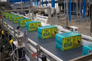 An image of boxes of Tiny Bomb beer cans on a conveyer belt in the WISEACRE brewing and packaging facility.