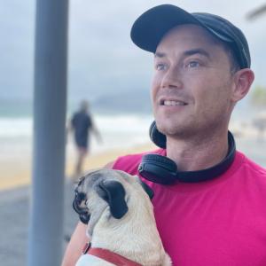 Author Adam Cox on the beach with a puppy who is a tiny 12-pud pug named Cindy Crawford (after the supermodel), after recently graduating from Harvard Business School but before earning his business law degree from Cornell started