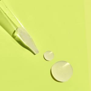 Close-up of a glass dropper, and two swatches of an off-white emulsion, on a light green background