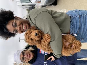The pet owner is smiling at the camera while holding his fluffy brown dog. An event volunteer smiles by her side.