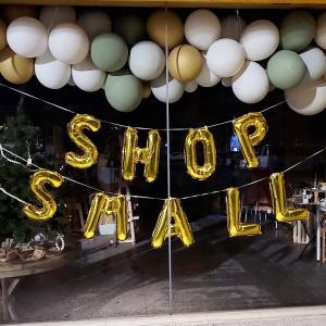 Showcase with a garland of green, gold and white balloons and below are balloons in gold letters spelling out the little shop