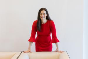 Jodi Daniels, founder of Red Clover Advisors, leans on a table in a red dress