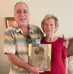 Adult son Floyd standing with his mother Rose Avillo smiling and holding a photo of her late husband in his military uniform.