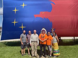 Representatives of World Spine Care Canada and the Global Spine Care Initiative stand with members of the Pimicikamak Omikawan in front of the band flag during the Mamawitenamatowin Summer Healing Camp in July 2022.