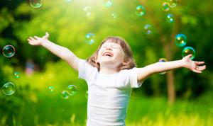 Girl smiling in sun with green background and bubbles floating to sky