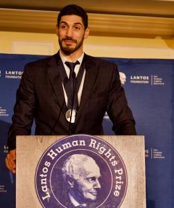 Enes Kanter Freedom stands at a podium with the Lantos Prize medal around his neck