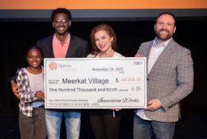 Dr. Crystal Morrison, Meerkat Village co-founder and CEO, stands in the center holding oversized UpPrize award check for $100,000.  She stands with her 13 yr old daughter Zoe and 17 yr old son Fikru (on the left in the picture) and her husband Dr. Justin 