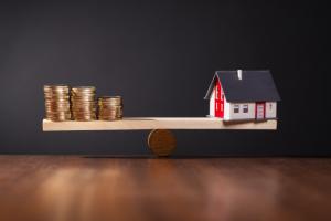 Seesaw with a house on one side and stacks with coins on the other.