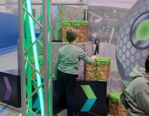 An attendee wielding a foam pick axe selects their choice of prize box from a wall of video game themed props.