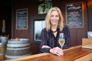 Woman smiles holding a glass of sparkling wine in what looks like a winery tasting room