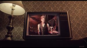 An old TV in a dingy room displays a man in a silver vest.