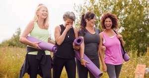 Women walking on a nature path while holding yoga mats, talking and smiling.