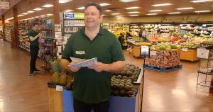 Photo of actor Angus Benfield as Jake,  once-successful PR specialist, now a stock boy in his mid-forties, in the "Yellow Bird" store handing out fliers. The photo is a still image from the The multi-award winning, family-friendly comedy "Yellow Bird," di