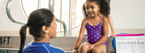 YMCA Hartley Dr woman swim instructor in the pool talking to young black girl sitting on pool edge  listening to her instruction