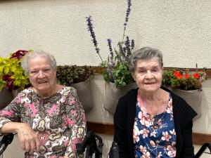Two seated smiling older women with a PLANTPOCKETS™ flower garden on the wall behind them.