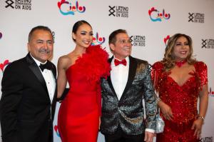 Guillermo Chacón is standing on the far left of the picture, he is wearing a black suit and comes to Miss Universe's shoulder. Guillermo is standing, smiling, with his arm around Miss Universe. Miss Universe is standing in between Guillermo and Dr. Melénd
