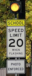 image of school speed sign with beacon flashing and "photo enforced" sign beneath