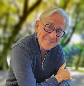 An image of Harry Hobbs wearing a blue sweater, standing outside, surrounded by nature.