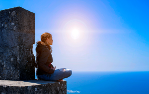 Young woman sits cross legged in meditation in front of the sea