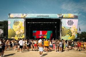 A crowd of people in front of a large stage with two mult-colored signs on the side with the new Lollapalooza branding.