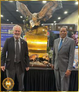 Michael Sheppard standing next to with Larry Elder in front of The Presidential American Patriot Life Size in bronze on display at FreedomFest 2023 in Memphis in the Treasure Investments Corporation Booth