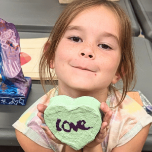 Young girl shows off a heart she painted at TAG with "love" written across the front.