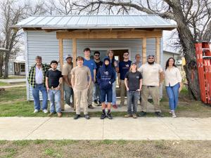 group of people of all ages in front of a small energy efficient home that they finished building.