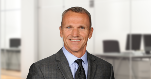 Sales executive Todd Grice stands smiling in front of blurred office background