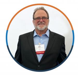 Mark walker is a Caucasian male wearing a dark suit, glasses and a conference badge around his neck. He is smiling. He stands against a white background