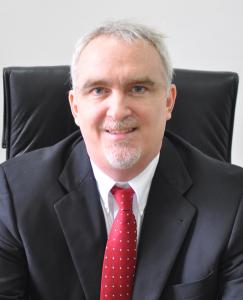 Head and shoulders shot of FINCA Impact Finance President and CEO Jeff Flowers wearing a dark grey suit, white collared shirt and red tie.