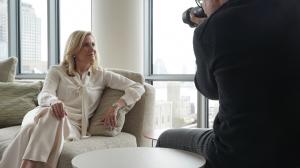 Anne Fink behind the scenes (seated on a couch with a photographer snapping her photo) for 21st Century Women: Twenty Years of Progress, photo by Randall Slavin.
