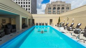 Rooftop pool with clear blue water, surrounded by loungers and cityscape views under a sunny sky.