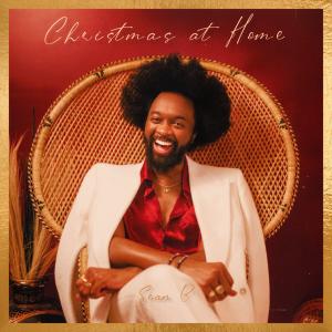 Sean B's cover for the Christmas at home album. Sean B is smiling sitting on a chair with holiday festive colors.