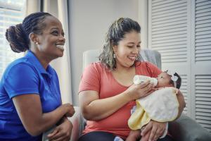 A home visitor smiling with mom holding her baby