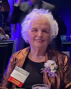 Mary Selz, co-founder of Thomas House Family Shelter, honored as Outstanding Founder, smiling at an award ceremony with a corsage and a name badge, exemplifying her dedication to philanthropy and community service.