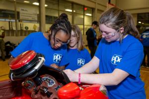 Three young girls modify a red electric ride-on car.