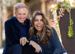 Mindy and Glenn Stearns sit smiling surrounded by trees and a garden.