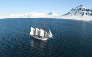 Tall sailing ship Linden in high arctic waters with snow topped mountains