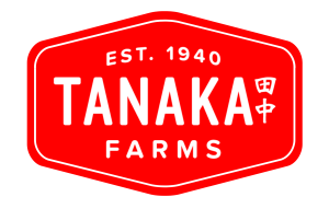 The Tanaka Farms logo is red with withe lettering. In the center in large white letters it spells out TANAKA. Next to the name Tanaka is the Japanese Kanji (symbol) for Tanaka, which translates to "middle of the field" in Japanese. Above the name Tanaka, 