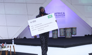 Emmanuel Adebayor carrying the fund-raising cheque on the runway at the Africa Fashion Unites showcase in Abidjan