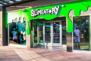 Slimeatory store front of the san tan village location. Big slime drips with the Slimeatory logo on top. double door entrance.