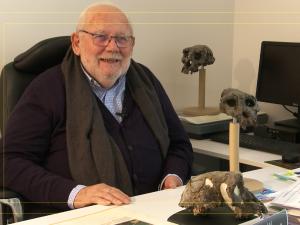 Dr. Michel Brunet sitting at desk with a copy of the Toumai skull on the desk. He was accused by his colleague, Dr. Alain Beauvilain, of fraud.
